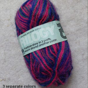May include: A ball of Trilogy yarn in shades of pink, blue, and green. The label reads "50% Wool, 50% Orlon Acrylic" and "Fashion story in 3 parts, each strand another color." The text "3 separate colors in one strand" is also visible.
