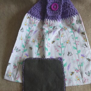 May include: Purple crocheted dish towel with a floral print and a purple button. The towel has a gray fabric insert.