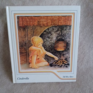 May include: A vintage children's book cover featuring an illustration of a young girl tending a fire in a stone fireplace. The book title is "Cinderella" and the series title is "Tell Me a Story".