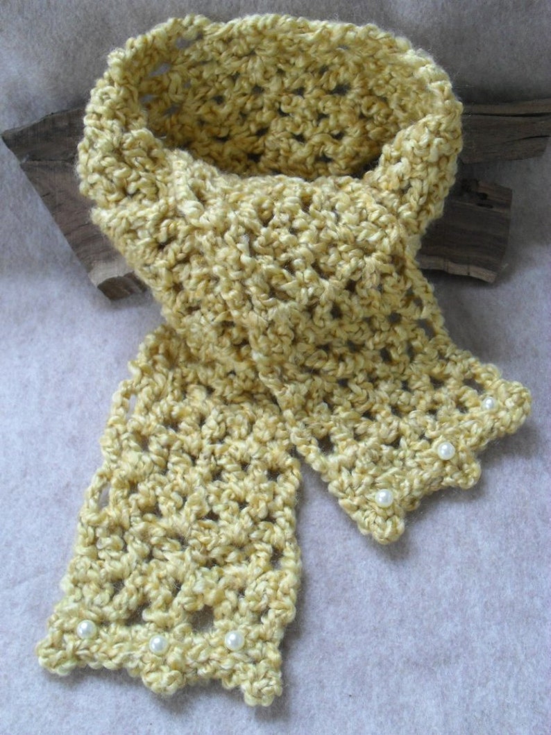 May include: A yellow crocheted scarf with a delicate openwork pattern and white pearl embellishments.