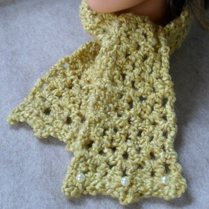 May include: A yellow crocheted scarf with white pearl accents. The scarf is made with a delicate stitch pattern and has a soft, textured look.