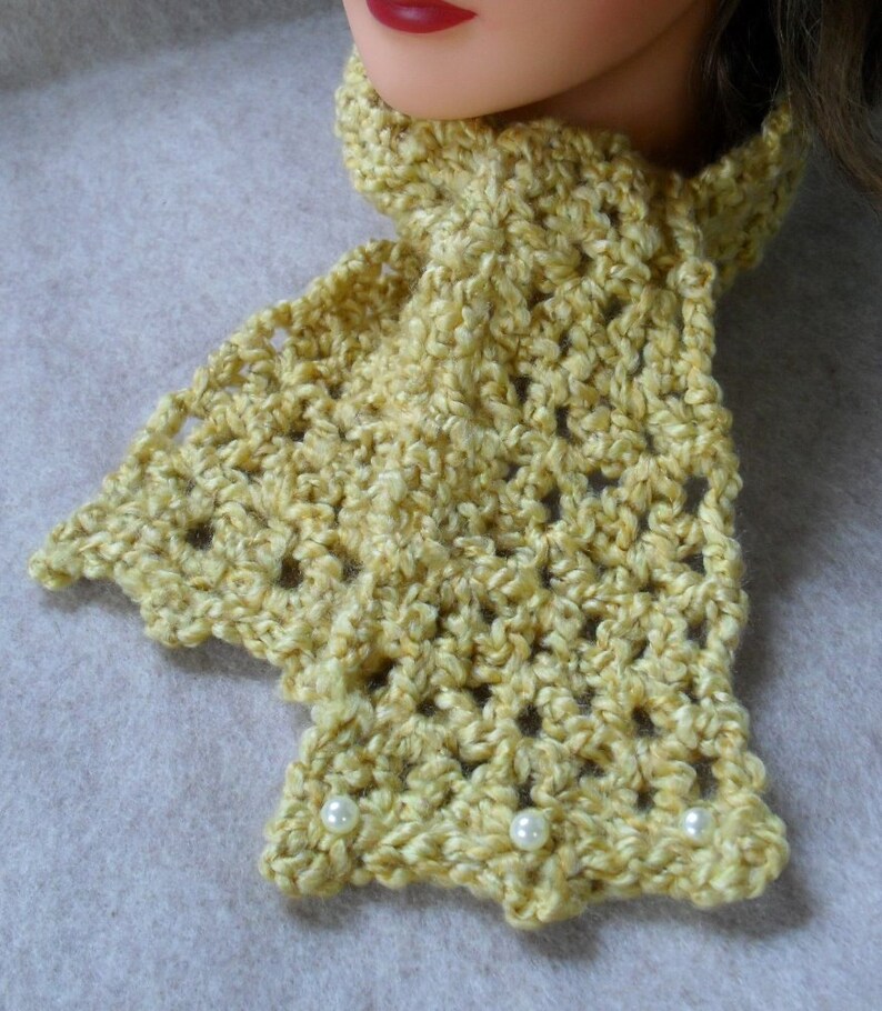 May include: A yellow crocheted scarf with white pearl accents. The scarf is made with a delicate stitch pattern and has a soft, textured look.