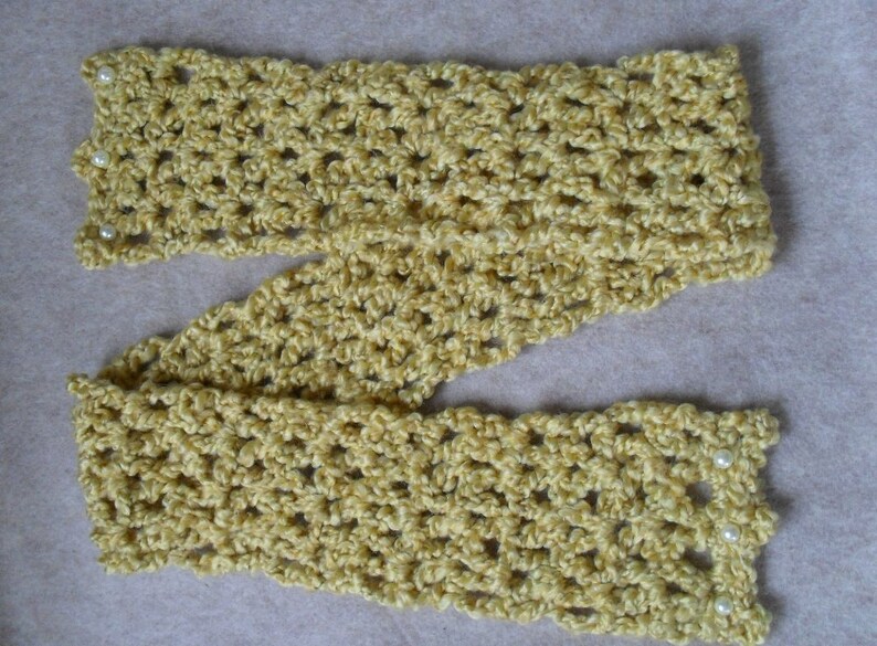 May include: A crocheted scarf in a light yellow color with white pearl accents. The scarf is made with a simple stitch pattern and has a delicate, feminine look.