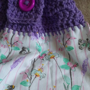 May include: Purple crocheted dishcloth with a pink button and a white fabric backing with a floral pattern.