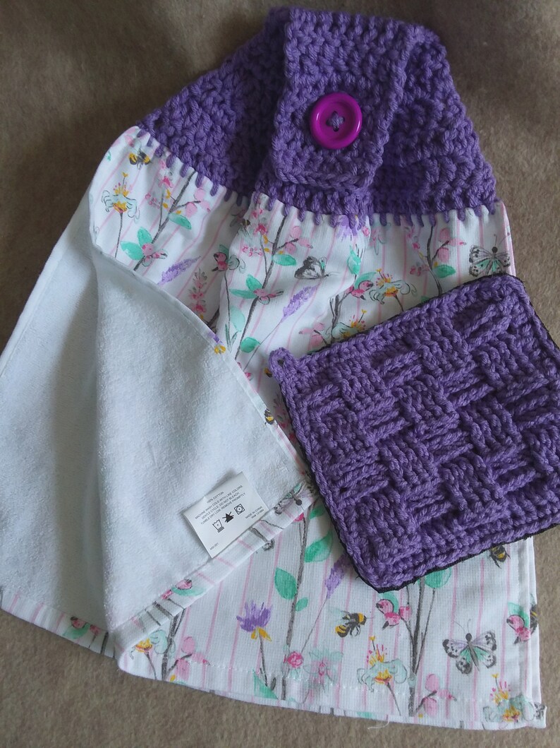 May include: Purple crocheted dish towels with a floral print and a purple button. The towels are made of cotton and are machine washable.