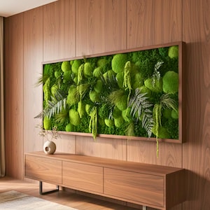 May include: A rectangular wall-mounted art piece featuring a dense arrangement of preserved green moss and various fern fronds encased in a thin wooden frame, displayed above a long, low wooden media console with three storage compartments.