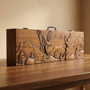 Könnte beinhalten: Eine rechteckige Holzkiste mit einem geschnitzten Relief, das Adler zeigt, die über einer Berglandschaft fliegen. Die Kiste hat einen Griff und Metallverschlüsse. Das Holz hat einen warmen, natürlichen Farbton, und die Schnitzdetails sind aufwendig.
