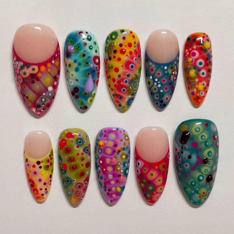 May include: A set of ten oval-shaped artificial nails, each with a unique, colorful design. The nails feature a variety of patterns, including dots and swirls, in shades of red, yellow, blue, green, and pink. Some nails have a nude-colored base.