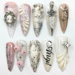 May include: Ten long, pointed acrylic nails with diverse designs. The nails are decorated with pearls, lace, miniature roses, and metallic details. One nail features the word "Angel".