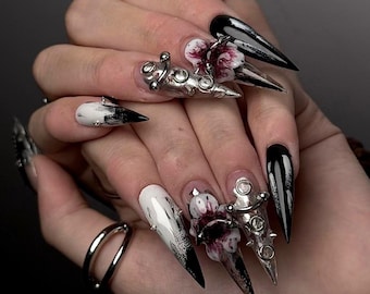 May include: Long stiletto-shaped artificial nails featuring a monochromatic black and white color scheme. The design includes three-dimensional silver metallic accents, embedded clear rhinestones, and detailed floral patterns with dark red accents.