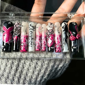 May include: A set of long, square-shaped artificial nails. The nails feature a variety of designs, including the word "Playboy", a bunny logo, zebra stripes, and rhinestones. Colors include black, white, and pink.