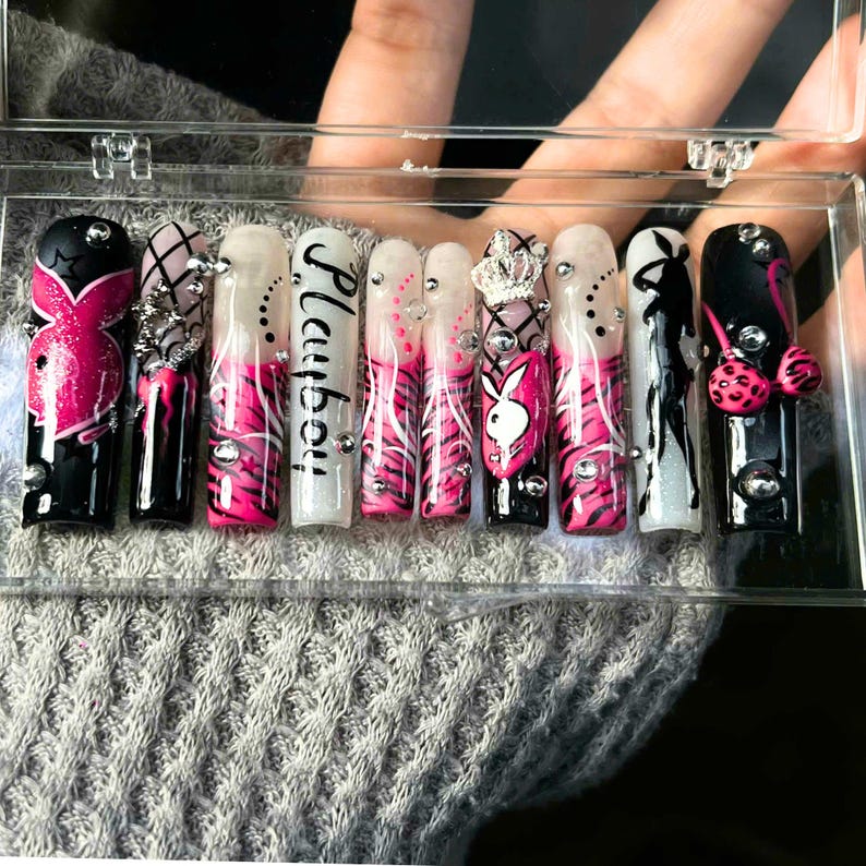 May include: A set of long, square-shaped artificial nails. The nails feature a variety of designs, including the word "Playboy", a bunny logo, zebra stripes, and rhinestones. Colors include black, white, and pink.