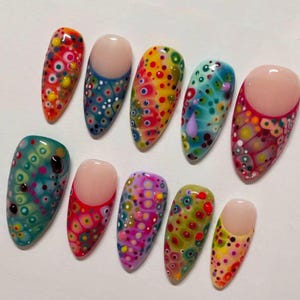 May include: A collection of ten artificial nails with a glossy finish. Each nail features a unique design of colorful, abstract patterns with a variety of dots and circles in shades of red, yellow, blue, and green. Some nails have a nude base.