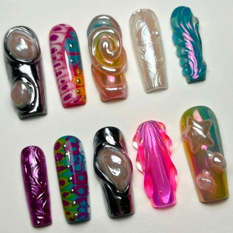 May include: A collection of ten artificial nails in various designs and colors. The nails feature a range of styles, including iridescent swirls, textured patterns, and metallic accents. Colors include pink, blue, green, and silver.