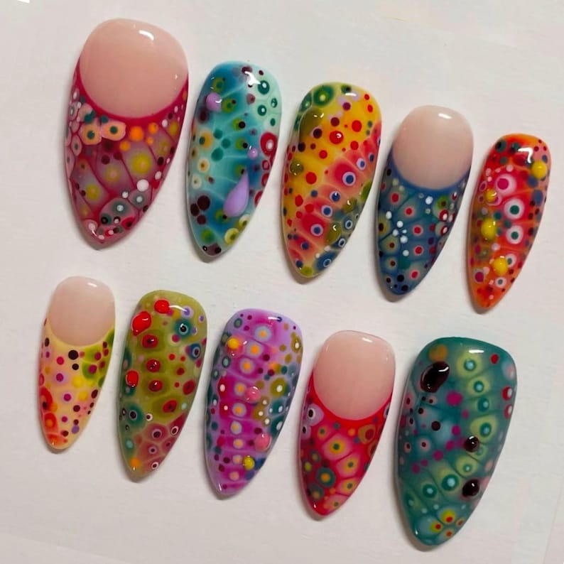May include: A set of ten artificial nails with colorful, abstract designs. Each nail features a different pattern of dots and circles in shades of red, yellow, blue, green, and purple. Some nails have a solid nude base.