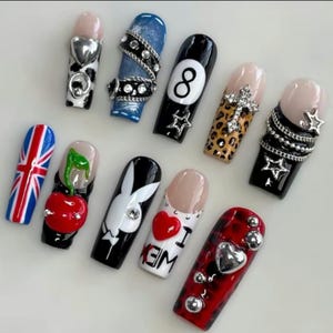 K&ouml;nnte beinhalten: Eine Sammlung k&uuml;nstlicher Fingern&auml;gel mit verschiedenen Designs. Die N&auml;gel zeigen eine britische Flagge, eine Kirsche, einen Playboy-Hasen und ein "I <3 EM"-Design. Andere N&auml;gel haben eine 8-Ball, Leopardenmuster und silberne Verzierungen.