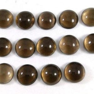 Puede incluir: Catorce cabujones redondos, lisos y translúcidos de color marrón, dispuestos en tres filas. Cada pieza presenta una superficie pulida y abovedada con un tono marrón oscuro constante y un brillo que crea un pequeño reflejo blanco.