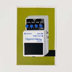 Puede incluir: Un pedal de efectos Digital Delay OD-3 gris y negro con perillas azules y texto blanco. El pedal tiene conectores de entrada y salida, y el texto "Digital Delay" se muestra de forma destacada. El fondo es verde oliva liso.