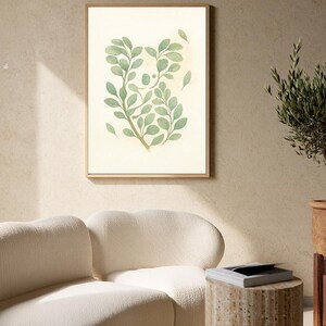 May include: A framed botanical print featuring a watercolor illustration of green leaves and stems. The artwork is set against a cream-colored background and framed in a light brown wooden frame. The print is displayed in a modern living space.