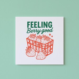 May include: Square white print with a green and red strawberry design. The text "FEELING Berry good" is written in green above a red illustration of strawberries in a basket. Two red stars are on the right side of the basket.