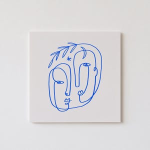 May include: A minimalist art print featuring a blue line drawing of two faces. The artwork is on a white background and includes a star and leaf-like details. The faces are stylized with simple lines, creating a modern and abstract aesthetic.