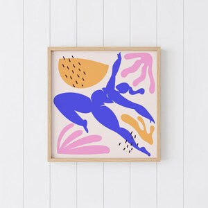 May include: A framed art print featuring a blue silhouette of a person in a dynamic pose, set against a cream background with abstract shapes in orange and pink. The artwork is enclosed in a natural wood frame.