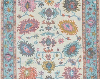 May include: Rectangular area rug with a cream-colored field and a turquoise border. The rug features a floral pattern in shades of pink, orange, blue, and purple. The design includes stylized flowers and vines.
