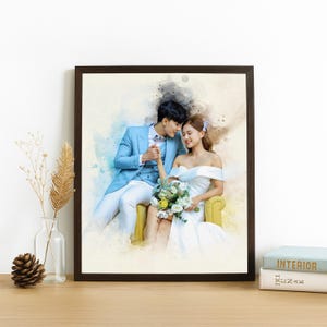 May include: A framed watercolour print depicting a couple in wedding attire. The man wears a light blue suit, and the woman is in a white off-the-shoulder dress. They are seated on a yellow chair, holding hands, with a bouquet of flowers.