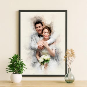 May include: A framed watercolour portrait of a smiling couple on their wedding day. The man wears a grey suit and the woman a white wedding dress, holding a bouquet of white flowers. The frame is black.