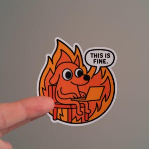 Peut inclure: Autocollant représentant un chien de dessin animé assis dans un fauteuil en feu devant un ordinateur portable. Une bulle de dialogue dit : « THIS IS FINE ». Le chien est orange et le feu est rouge et jaune.