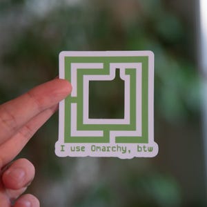 Könnte beinhalten: Ein quadratischer Aufkleber mit einem grünen Labyrinth-Design und einer Flaschenform in der Mitte. Der Aufkleber hat den Text "I use Omarchy, btw" am unteren Rand. Der Aufkleber wird von einer Hand gehalten.