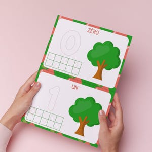 May include: A children's learning book open to two pages. The pages display the numbers zero and one, with dotted lines for tracing. Each page has a green tree illustration and the French words "Zéro" and "Un".