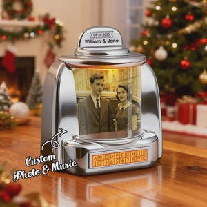 Op de afbeelding: Een verchroomd fotolijstje in retrostijl met een foto van een stel. De lijst heeft een digitaal display met de tekst "ABCDEFGHIJK 12345678910". De bovenkant van de lijst heeft de tekst "09-24-2025 William & Jane". De lijst heeft ook de tekst "Custom Photo & Music".