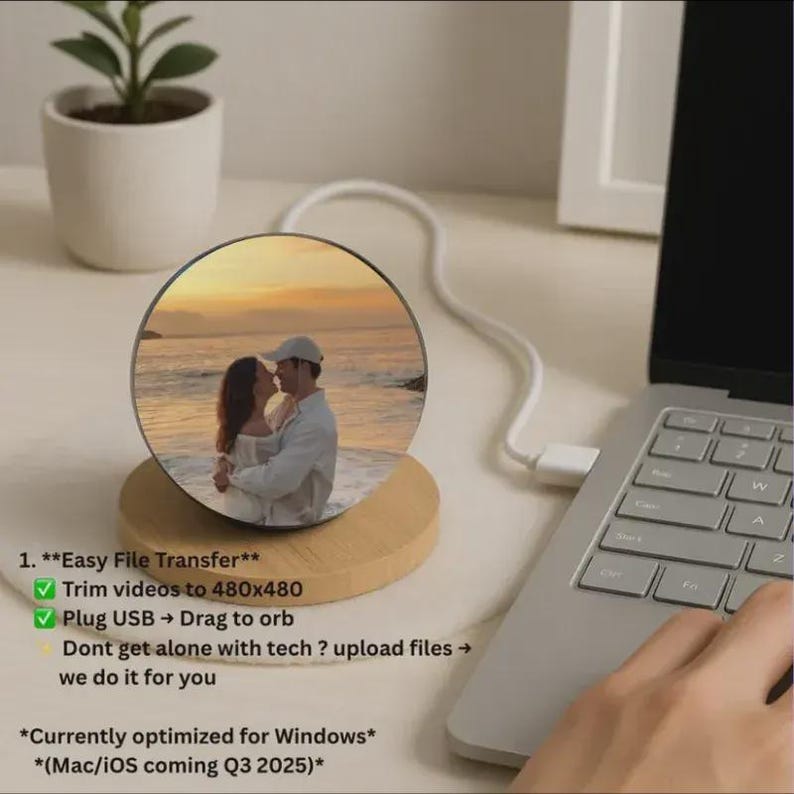 Puede incluir: Una pantalla redonda para fotos con una imagen de una pareja en la playa. La pantalla est&aacute; sobre una base de madera y conectada a un port&aacute;til por USB. El texto dice "Easy File Transfer" y "Trim videos to 480x480".