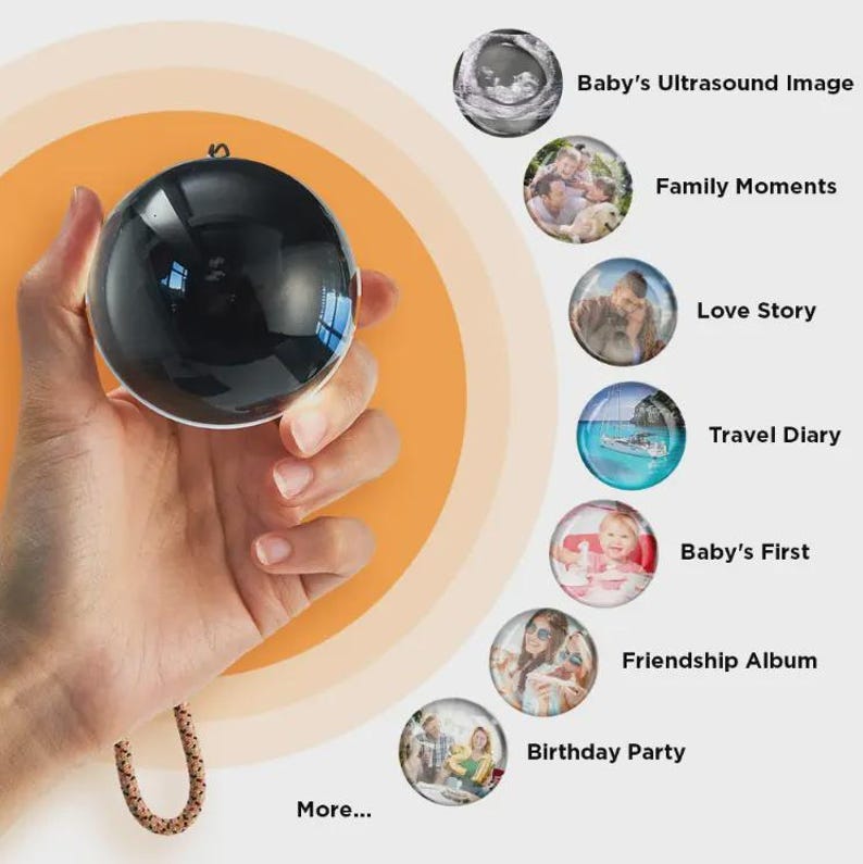 Puede incluir: Un adorno esf&eacute;rico negro con una superficie reflectante se sostiene contra un fondo naranja. El adorno est&aacute; suspendido por un cord&oacute;n decorativo. La imagen presenta miniaturas circulares con texto: "Baby's Ultrasound Image", "Family Moments" y "Love Story".