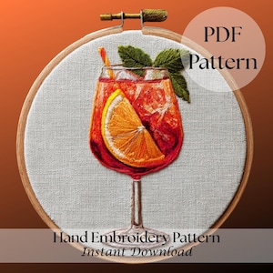 Könnte beinhalten: Handstickmuster mit einem Cocktail in einem Glas mit einer Orangenscheibe, Eis und einem Strohhalm. Das Design befindet sich auf einem weißen Stoff, der in einem hölzernen Stickrahmen gespannt ist. Der Text lautet "PDF Pattern" und "Hand Embroidery Pattern Instant Download."