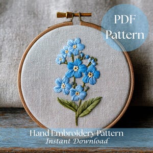 Op de afbeelding: Een handborduurpatroon met een bloemmotief van blauwe vergeet-mij-nietjes met gele centra en groene bladeren, geplaatst in een houten borduurring. De tekst "PDF Pattern" en "Hand Embroidery Pattern Instant Download" zijn ook zichtbaar.