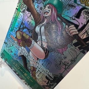 Puede incluir: Una tarjeta coleccionable hologr&aacute;fica con una ilustraci&oacute;n de personaje. El personaje es una mujer con cabello rosado, que lleva un sombrero verde, una chaqueta marr&oacute;n y una blusa blanca. La tarjeta tiene texto japon&eacute;s y un contador +1000.