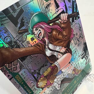 Puede incluir: Carta coleccionable hologr&aacute;fica con una ilustraci&oacute;n de estilo manga de un personaje con cabello rosado, un sombrero verde y una chaqueta marr&oacute;n. La tarjeta tiene texto japon&eacute;s y una potencia de 6000. El fondo presenta paneles de estilo c&oacute;mic.