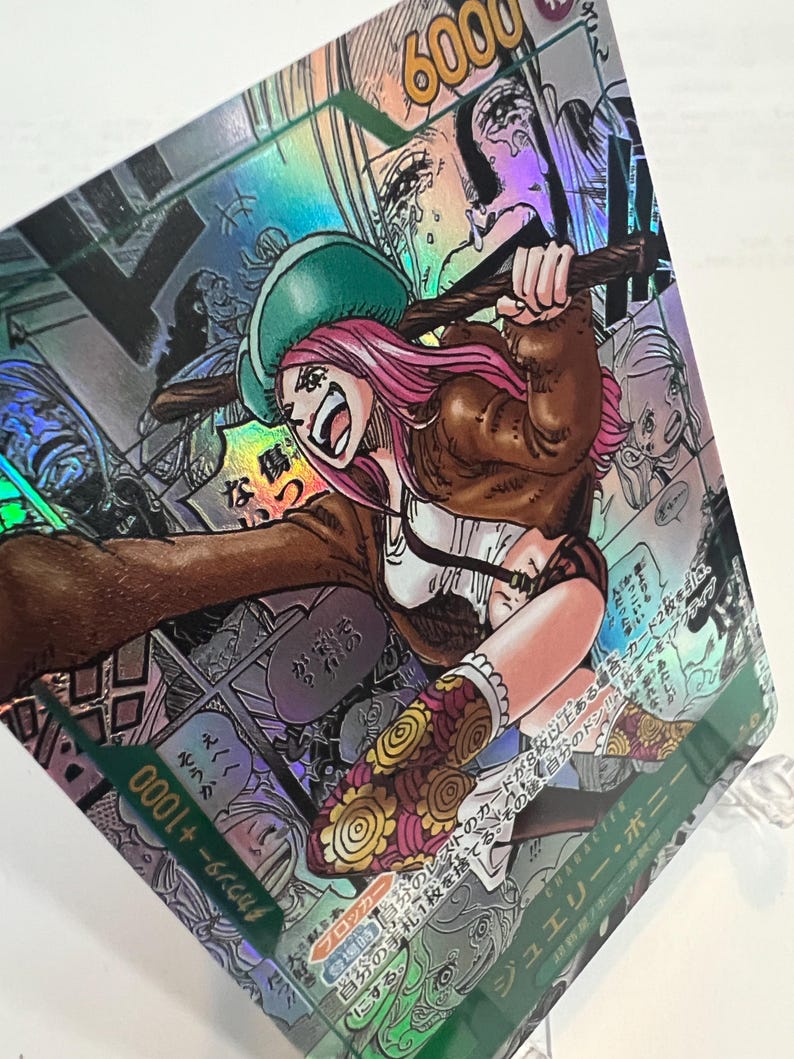 Puede incluir: Carta coleccionable hologr&aacute;fica con una ilustraci&oacute;n de estilo manga de un personaje con cabello rosado, un sombrero verde y una chaqueta marr&oacute;n. La tarjeta tiene texto japon&eacute;s y una potencia de 6000. El fondo presenta paneles de estilo c&oacute;mic.