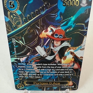 Peut inclure: Une carte à collectionner avec Portgas D. Ace d'Alabasta/Whitebeard Pirates. La carte a une bordure dorée et un design holographique avec une illustration de personnage. Le texte de la carte comprend "COUNTER +1000" et "5000 SPECIAL".