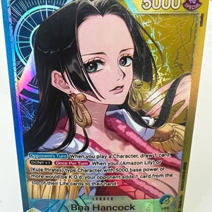 May include: A trading card featuring Boa Hancock from the One Piece series. The card has a holographic background with a portrait of the character. The card's text includes the character's name, leader designation, and game instructions. The card has a 5000 power rating.