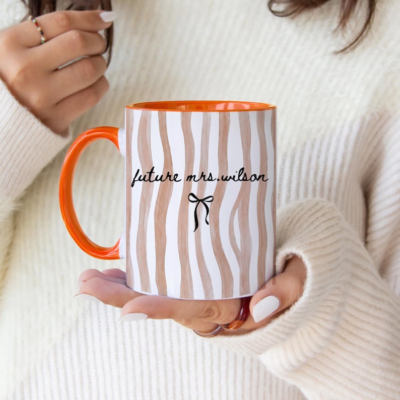 May include: A white ceramic mug with a black handle and the text "But First, Coffee" in a handwritten style. The mug is on a white surface. The mug is approximately 4 inches tall.