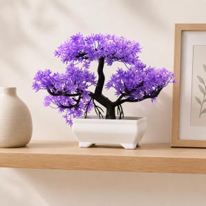 May include: A decorative artificial bonsai tree featuring vibrant purple foliage and a dark brown trunk. The tree is potted in a rectangular white ceramic container with four small feet, creating a structured and balanced appearance for display.