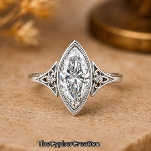 Könnte beinhalten: Ein silberfarbener Ring mit einem großen, klaren, marquise-geschliffenen Mittelstein in einer Fassung mit Milgrain-Details. Die Ringschiene zeigt auf beiden Seiten komplexe, durchbrochene Metallmuster, die jeweils mit einem kleinen, runden Stein besetzt sind.