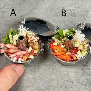 May include: Miniature silver hot pot with a variety of ingredients, including shrimp, mushrooms, and vegetables. The pot has a central chimney and is topped with a silver lid. The image shows two hot pots.
