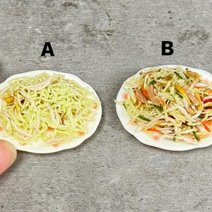 May include: Miniature plates of salad, labeled A and B. Plate A features shredded cabbage with a light dressing. Plate B includes shredded cabbage, ham, carrots, and green vegetables. Both plates have a white scalloped edge with floral accents.