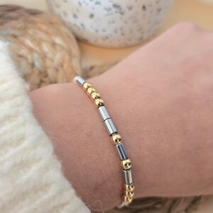 Puede incluir: Una pulsera de cuentas con cuentas doradas y plateadas alternas. La pulsera está ensartada en un cordón blanco y se lleva en la muñeca. El diseño es sencillo y elegante, adecuado para el uso diario. Las cuentas son probablemente de metal.