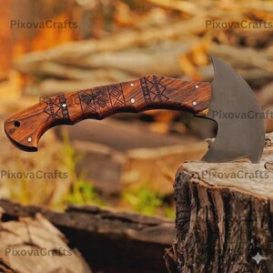 May include: A handcrafted axe with a dark, curved blade and a wooden handle. The handle features intricate carved patterns and a curved design for a secure grip. The axe is shown resting on a tree stump.
