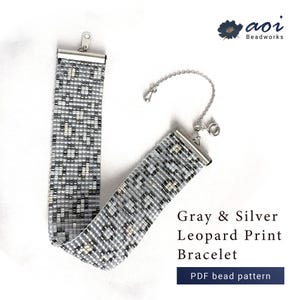Puede incluir: Una pulsera de cuentas con estampado de leopardo en gris y plata, con un patrón tejido de acentos metálicos, terminales de metal plateado y una cadena extensora. La imagen incluye el texto Aoi Beadworks y Gray & Silver Leopard Print Bracelet PDF bead pattern.